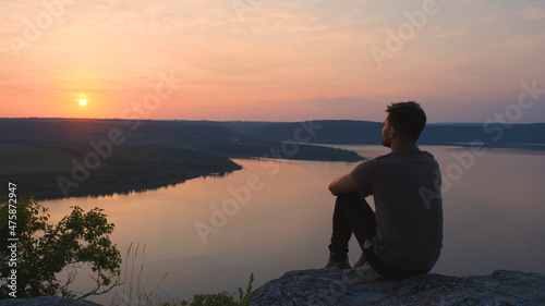 The young man sitting on rocky mountain above the beautiful river