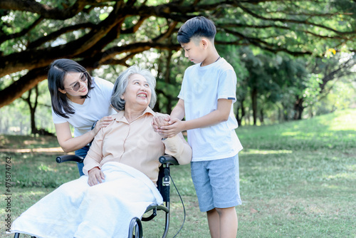 Asian elderly woman sitting in a wheelchair, smiling and happy with her daughter and grandson taking care of her, to relationship of Asian family and retirement age concept.