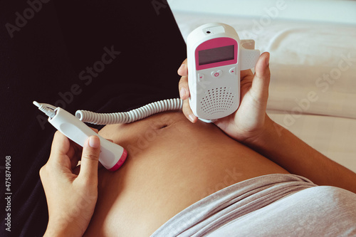 Tableau sur toile The close up pregnant woman using pocket fetal doppler to monitor baby heart beat
