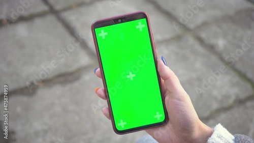 Woman holds mobile phone and swipes photos or pictures outside on a cold autumn day. Use a vertical green screen for copy space closeup. Chroma key mock-up on smartphone in hand. Surfing Internet 4k