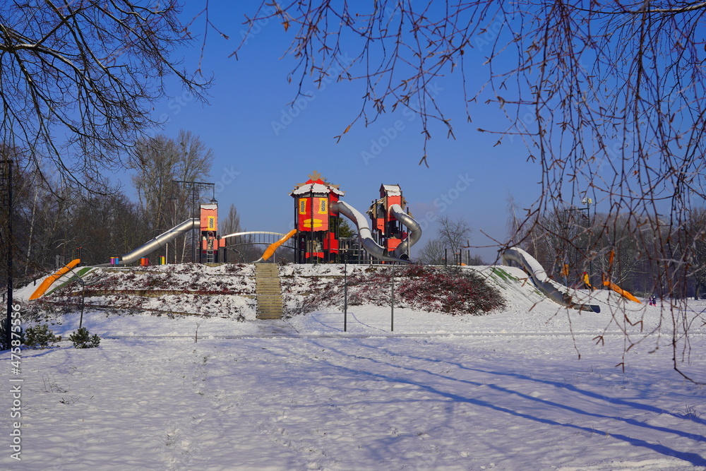 Naklejka premium Children's playground in a winter setting. Children's playground in a winter scenery. Family outdoors on a frosty sunny day 
