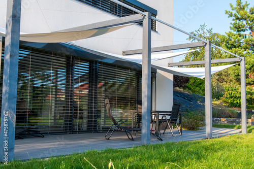 Detail of terrace of modern, white, cube, elegant, minimalist style passive house with large panoramic windows, grey shutters in maintained garden.