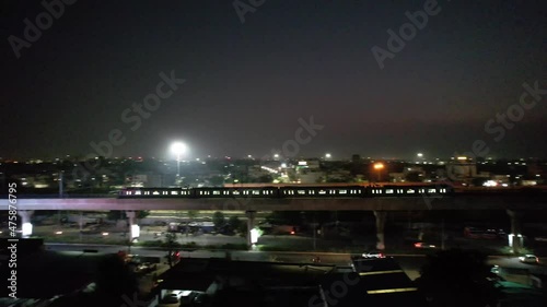 long distance right to left pan showing metro train on elevated bridge moving across the screen showing the dark cityscape of jaipur showing traffic and the dusk colors and public transport photo