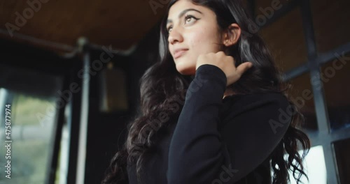 An Indian female with long brunet hair and black clothes standing and posing