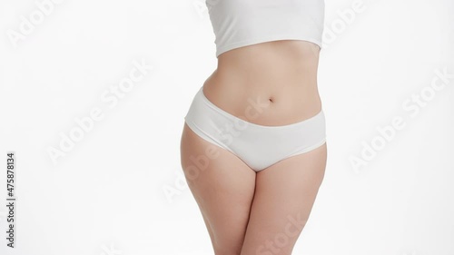 Horizontal medium shot of white-skinned plus size woman with long brown hair in white underwear turns to the camera on white background | Anti cellulite commercial