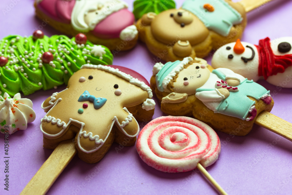Cookies on sticks in a shape of Santa Claus, elf character, Gingerbread man, snowman, bear, New Year 2022 tree, lollipop on purple background top view. Cute treats, sweets, candies for Christmas fun.