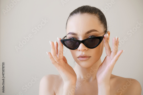 Woman face in sunglasses. Girl face close up portrait of woman. Young girl on light background touches his glasses with his hands. Concept - sale of sunglasses. Wearing sun protection glasses.