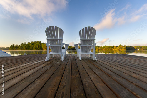 Empty Adirondack chairs on a wooden dock on a lake in Muskoka, Ontario Canada during the summer.