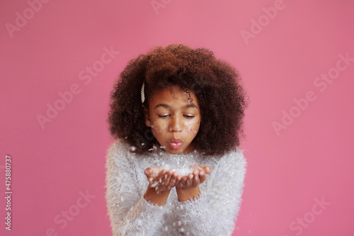 Lovely teenage girl with bright festive makeup blowing on the snow in her palms