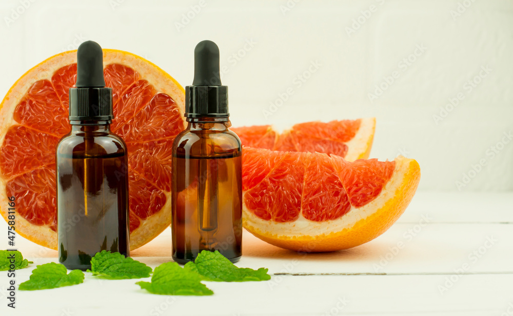 two cosmetic bottles with a brown glass dropper with a grapefruit fruit cosmetic for natural skin care of the face and body. close angle. two cosmetic bottles with a brown glass dropper with a grapefruit fruit cosmetic for natural skin care of the face and body. close angle.