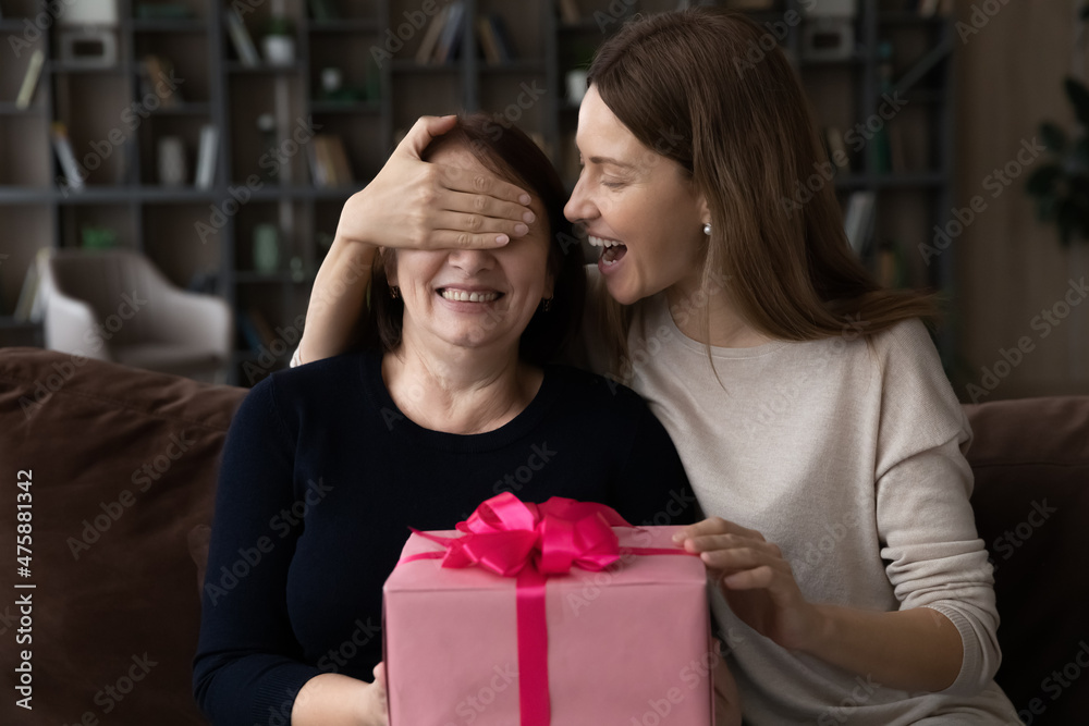 Surprise for mommy. Loving grownup daughter close retired mother eyes with palm make present on holiday birthday 50s 60s anniversary. Amazed aged mom receive gift of dream from adult kid on Women Day