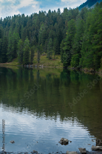 Blick auf einen grün schimmernden See. Gelegen in einem Nadelwald, mit Spiegelungen auf dem Wasser