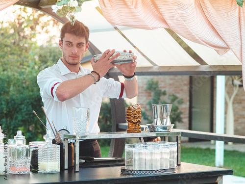 Sticker Young attractive Caucasian barman shaking a cocktail at an outdoor party around