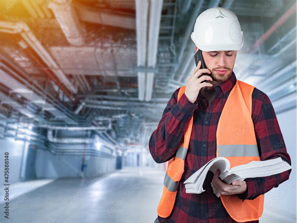 Engineer stands under pipes of ventilation system. Engineer with papers in his hands. Worker is talking on phone. Caridors with ventilation pipes. Concept development of vinthellation system Engineer stands under pipes of ventilation system. Engineer with papers in his hands. Worker is talking on phone. Caridors with ventilation pipes. Concept development of vinthellation system