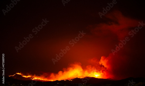 Wildfire engulfs small mountain area next to community.  Billowing smoke clouds fill the air © ecummings00
