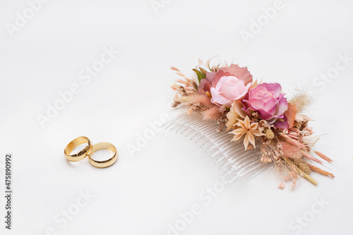 Pink flower buckle and two golden wedding rings on white background.