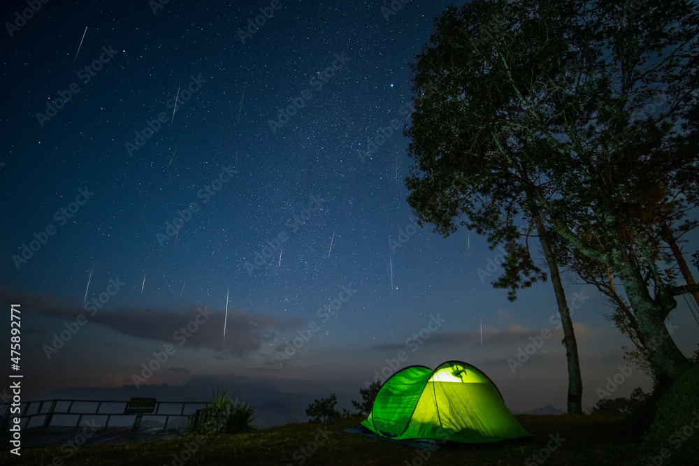 The Geminids Meteor Shower over a mountain with green glowing camping tent. Geminid Meteor in the dark night sky