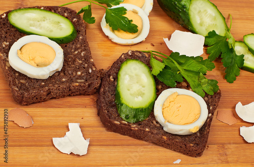 Slice of bread with egg, cucumbers and leaf of parsley on cutting board
