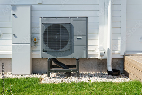Air source heat pump installed on the exterior of a modern wooden house. Air source heat pump reduces heating costs and your home\'s carbon footprint.