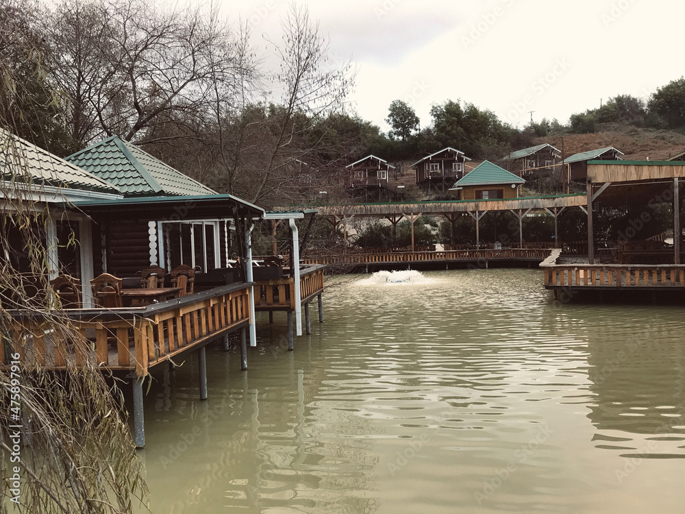 Fototapeta premium Street cafe with simple wooden interior on the shore of a picturesque lake. Authentic cafe with wooden tables and chairs near the Achigvar lake. Part of the terrace of the summer restaurant behind a w