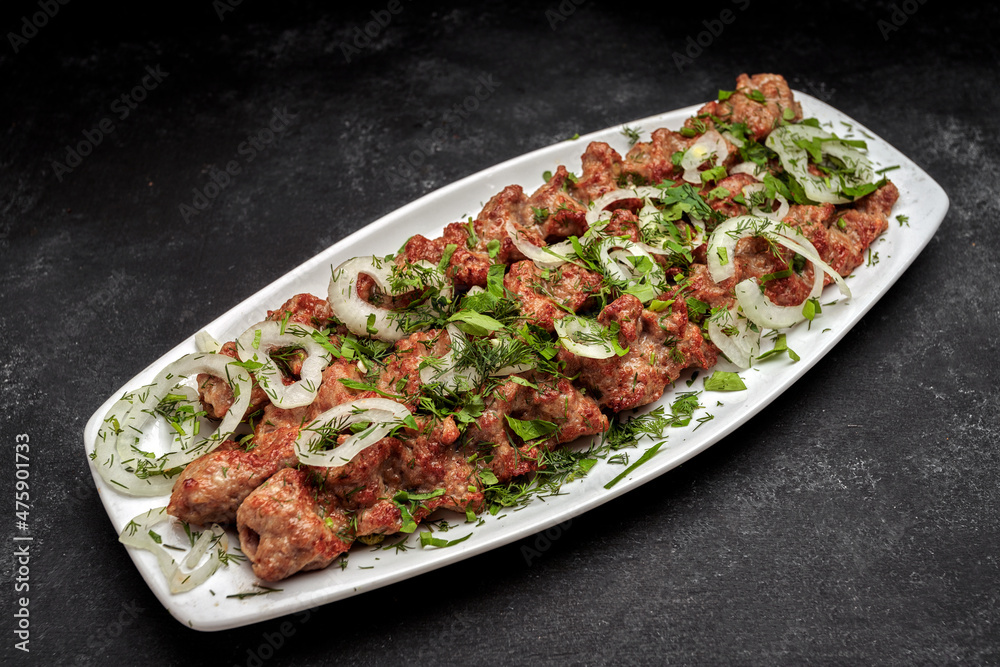 LULYA-KEBAB with herbs and onions on a plate, on a dark background