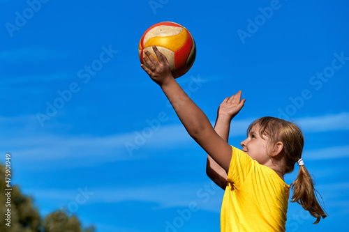 A girl is playing volleyball . The child hits the ball with his hand . Outdoor play © Alex Chebak
