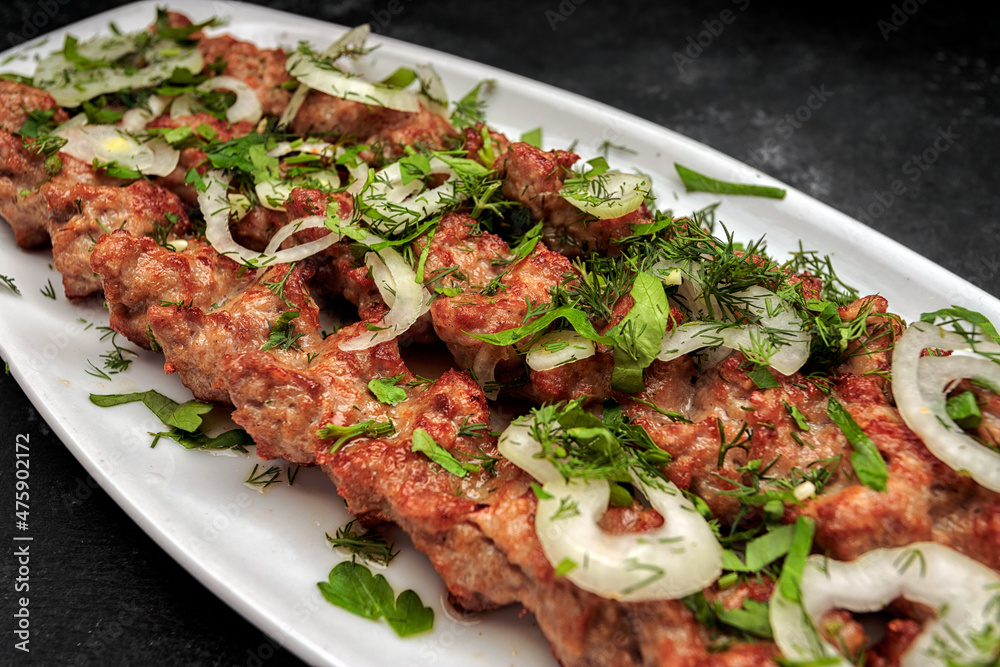 LULYA-KEBAB with herbs and onions on a plate, on a dark background LULYA-KEBAB with herbs and onions on a plate, on a dark background