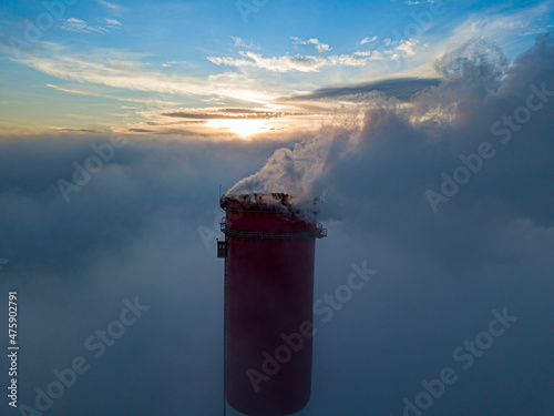 High chimney of a thermal power plant above the fog in the rays of the sunset. Aerial drone view.