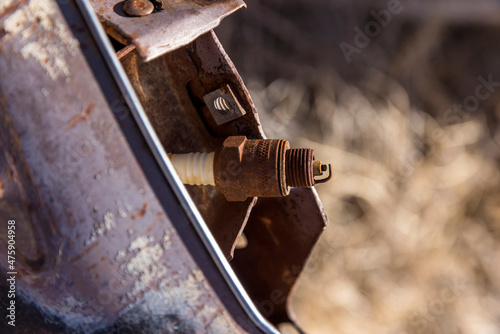 Rust covered spark plug rests on a piece of old car engine photo