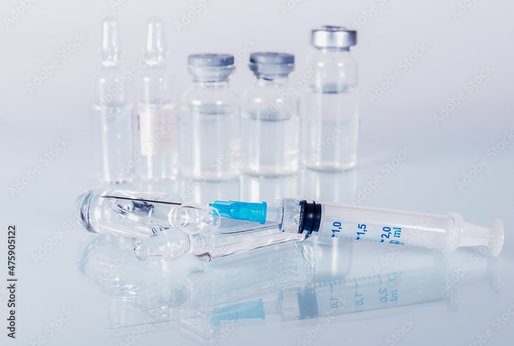 syringe and diferent kind of ampoules and vials close-up on white background with reflection