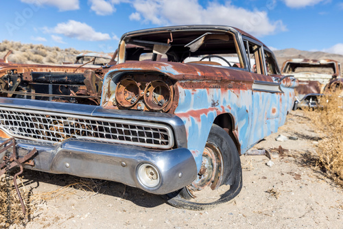 Blue and rust colored full body of vintage car with flat tires and missing hood abandoned in the nevada desert