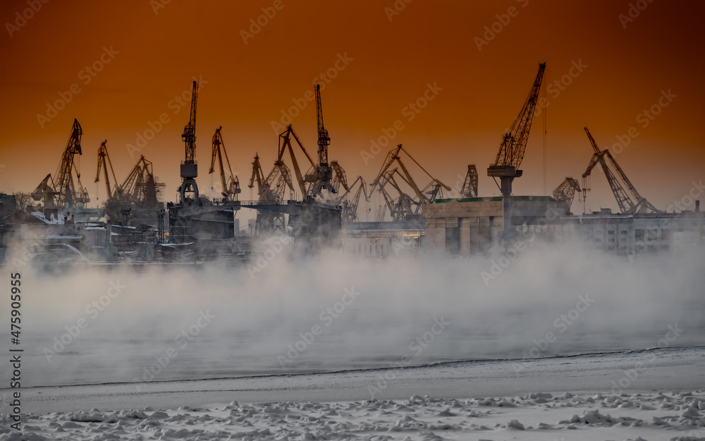 The construction of nuclear icebreakers at magic sunset, cranes of of the Baltic shipyard in a frosty winter day, steam over the Neva river, smooth surface of the river, sky of orange color