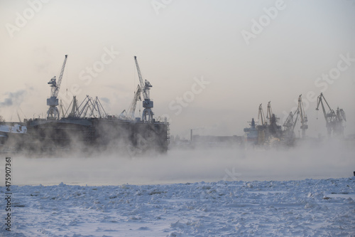 The construction of nuclear icebreakers, cranes of of the Baltic shipyard in a frosty winter day, steam over the Neva river, smooth surface of the river