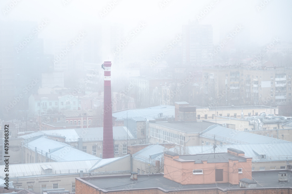 A man works at a height serving a thermal power plant CHP in a foggy city.