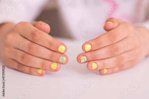 Little girl hands with beautiful manicure nails, yellow gel polish, flower design