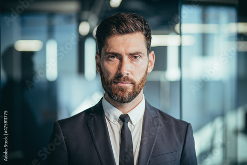 Portrait of a successful boss, photo of a close businessman, successful and pensive looking at the camera, a man with a beard in a modern office