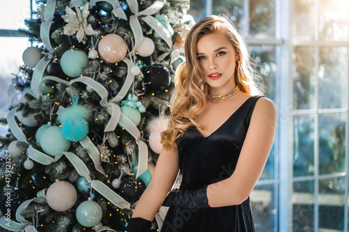 Beautiful woman in evening dress celebrates Christmas in luxurious apartments decorated christmas lights.