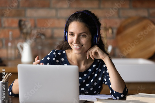 Happy millennial latin woman in headphones holding video call conversation, talking communicating distantly with tutor or mentor, improving professional knowledge distantly, e-learning at home.