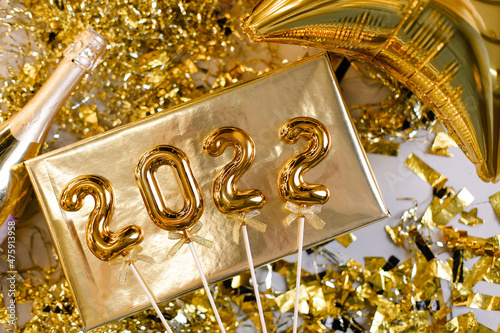 Happy new year 2022 concept. Foil gold numbers 2022 top view. Festive texture. Congratulatory card. Golden glitter metallic. Gift box, balloon and champagne
