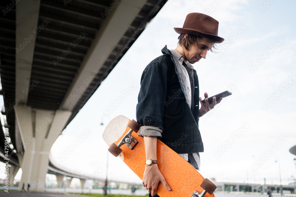 Skateboarding in the city and surfing in the phone browser. Milinal is a young man in a hat and a denim jacket. Skateboarding in the city and surfing in the phone browser. Milinal is a young man in a hat and a denim jacket.