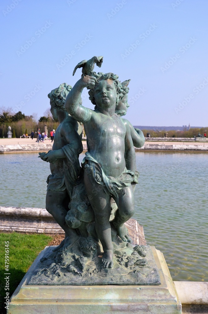 Bronze statue of three cherubs on the edge of a basin of the Bassin du Midi in the gardens of Versailles, in front of the west facade of the Palace of Versailles