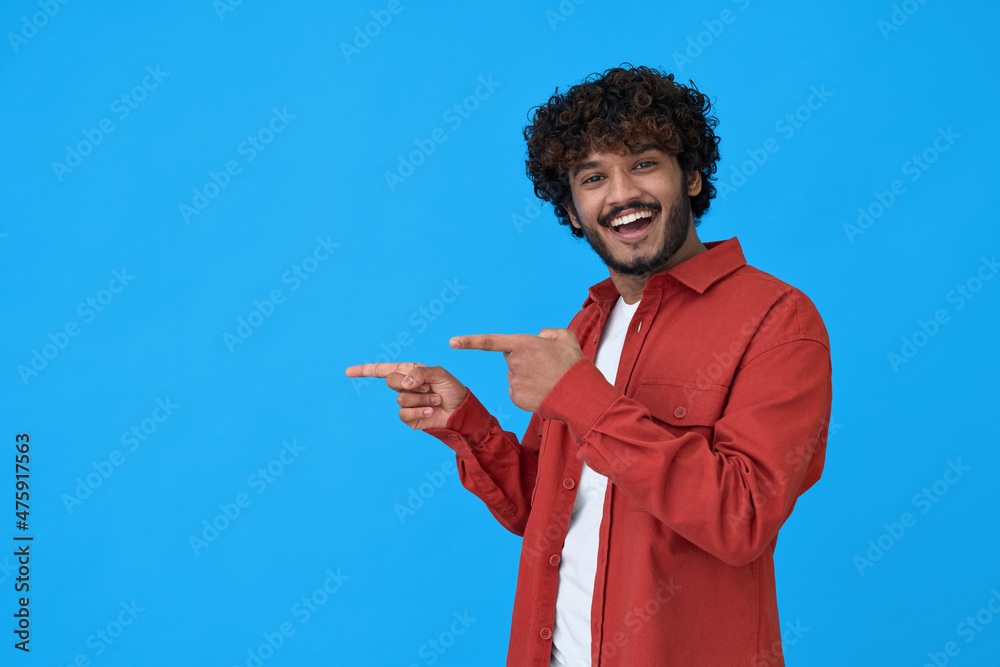 Φωτογραφία Happy excited young indian man looking at camera pointing aside with fingers hand gesture at copy space advertising new promotion, presenting sale offer standing isolated on blue background