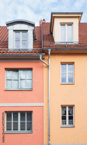 Two rows of 3 windows from two colorful buildings and a drain pipe in the middle of the facade