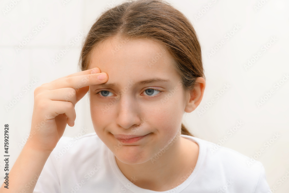 face of teenage girl, she looks at herself in the mirror and touches her face with her hand, she is upset and has frustrated emotions face of teenage girl, she looks at herself in the mirror and touches her face with her hand, she is upset and has frustrated emotions