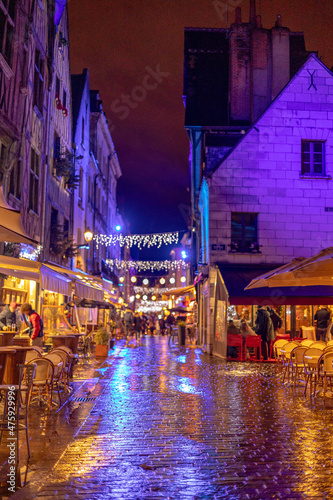 Place Plumereau - the square of medieval architecture built of half-timbered houses decorated of Christmas illuminations at the rain. Focused on the wet cobblestones in the foreground. Tours, France.