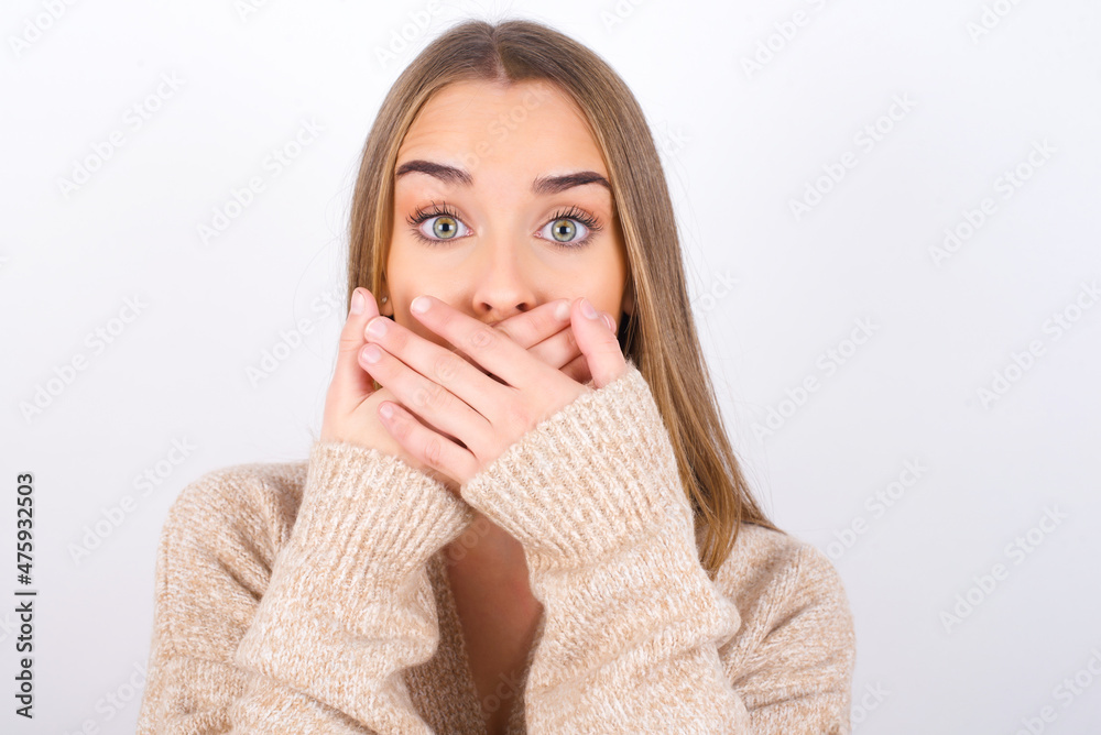 young caucasian girl wearing knitted sweater over white background shocked covering mouth with hands for mistake. Secret concept. young caucasian girl wearing knitted sweater over white background shocked covering mouth with hands for mistake. Secret concept.