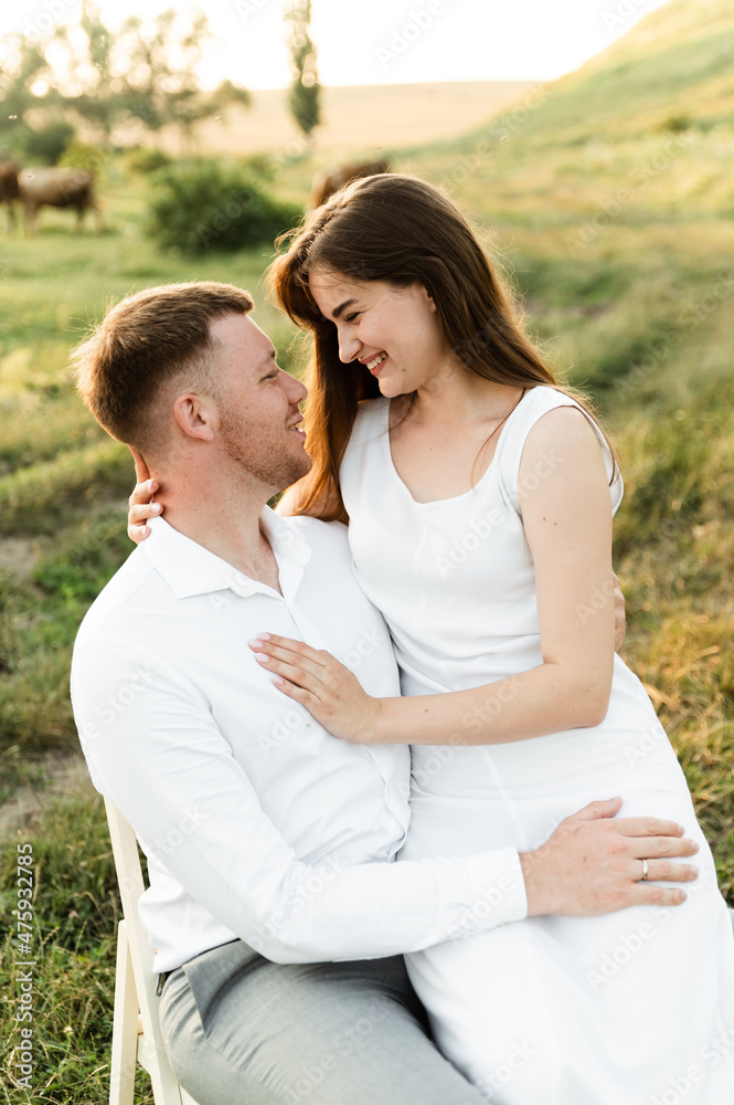 the newlyweds are sitting on a chair and hugging tenderly. girl with a boyfriend on a romantic date at sunset of the day. beautiful couple in the field. the newlyweds are sitting on a chair and hugging tenderly. girl with a boyfriend on a romantic date at sunset of the day. beautiful couple in the field.