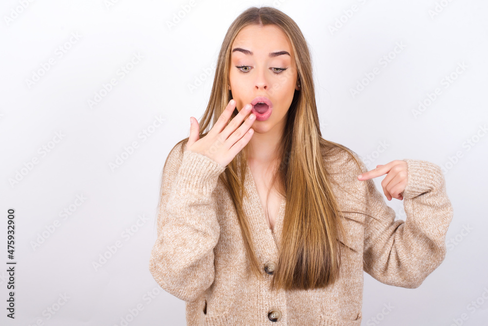 Shocked young caucasian girl wearing knitted sweater over white background look surprisedly down, indicates at blank with fore finger, Scared model Shocked young caucasian girl wearing knitted sweater over white background look surprisedly down, indicates at blank with fore finger, Scared model