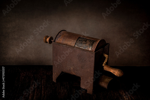 Still life with rustic rusty coffee roaster on vintage grunge background. Side view, cross light. Old tools and house appliances concept.