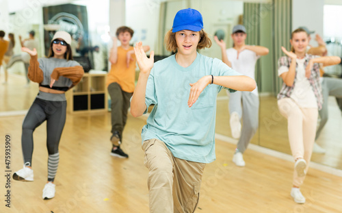 Fototapeta Naklejka Na Ścianę i Meble -  Portrait of cheerful teenage boy practicing hip-hop movements during group dance lesson in studio.